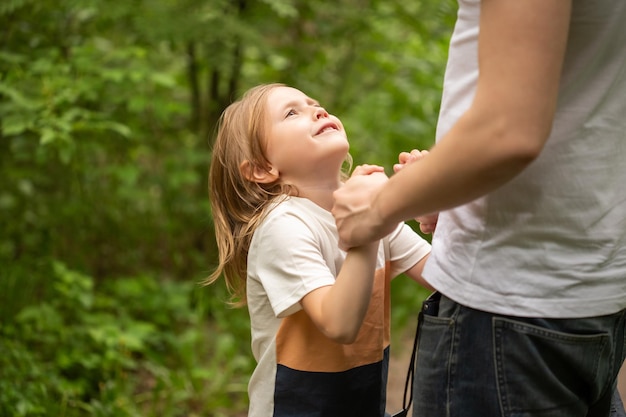 Papa et sa fille se promènent dans la forêt en été, la fille tient la main de papa et le regarde dans les yeux