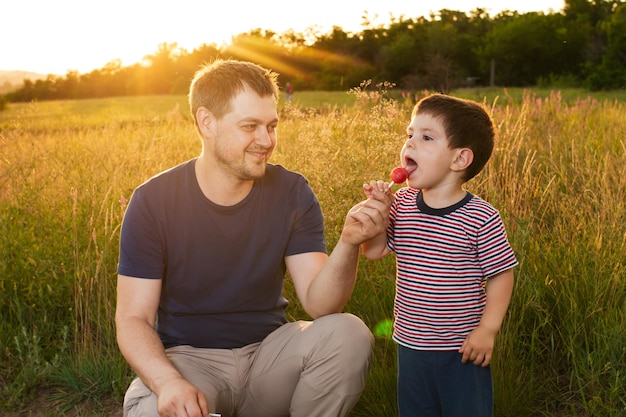 Papa et son fils marchent dans un champ d'été jaune le soir au coucher du soleil et mangent des bonbons sur un bâton La fête des pères aime dans la famille le rôle du père dans l'éducation de l'enfant