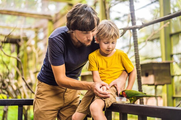 Papa et son fils nourrissent le perroquet dans le parc Passer du temps avec le concept des enfants