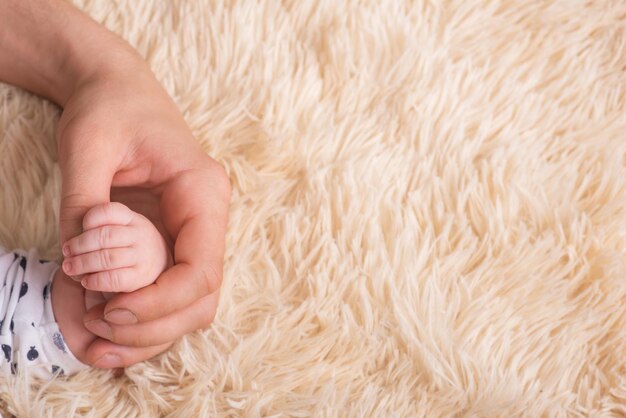 Papa tient dans ses mains une petite main de bébé. Petite main d'un nouveau-né dans les grandes mains fortes de papa. Massage des mains de bébé. Le bébé tient le doigt du père avec sa main. Place pour le texte, copyspace