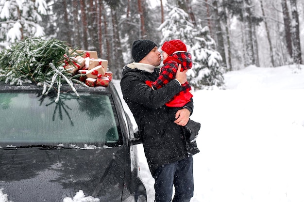 Papa tient sa fille à côté de la voiture et du sapin de Noël