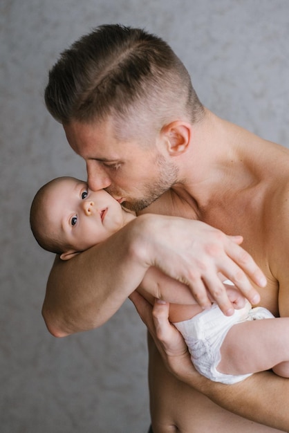 Papa tient son bébé dans ses bras à la maison et l'embrasse sur la joue