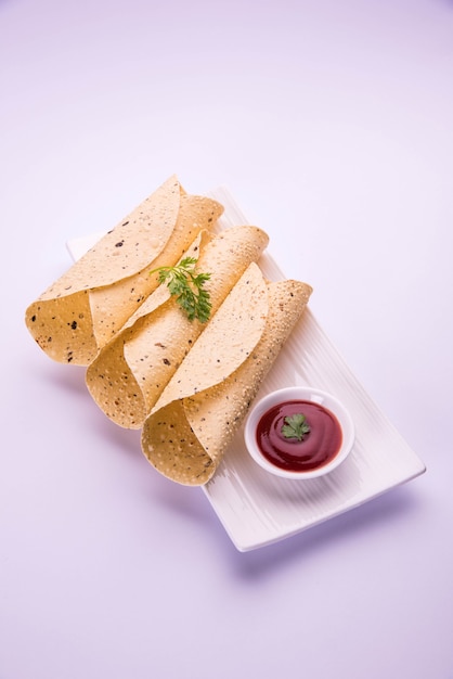 Le papad en rouleau rôti est un plat d'accompagnement ou d'accompagnement traditionnel indien, servi avec du ketchup à la tomate sur un dessus de table coloré ou en bois. Mise au point sélective