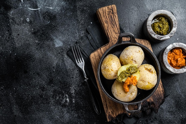 Papas arrugadas Îles Canaries Pommes de terre ridées avec sauces vertes et rouges servies dans une poêle Fond noir Vue de dessus Espace de copie