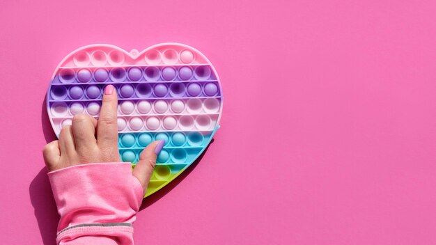 Pape en forme de coeur jouet anti-stress avec main féminine. Fidget sensoriel simple aux couleurs de LGBT. Mise à plat sur papier rose avec espace de copie. Aide au développement de la motricité des doigts.