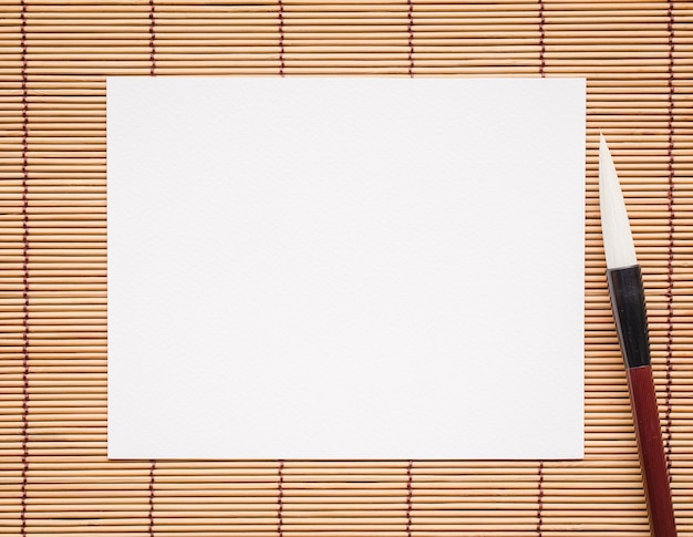 Photo papier blanc abstrait avec pinceau de calligraphie en bambou sur une image d'arrière-plan de natte de bambou pour ajouter du texte ou une carte de voeux nouvel an chinois papier de texte de peinture traditionnelle chinoise
