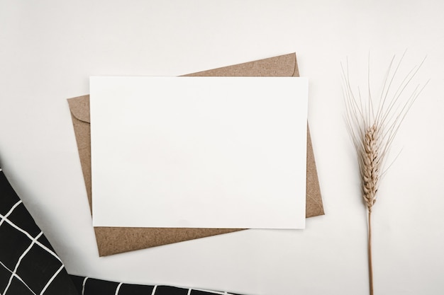 Papier blanc vierge sur enveloppe de papier brun avec fleur d'orge sèche et tissu noir avec grille blanche