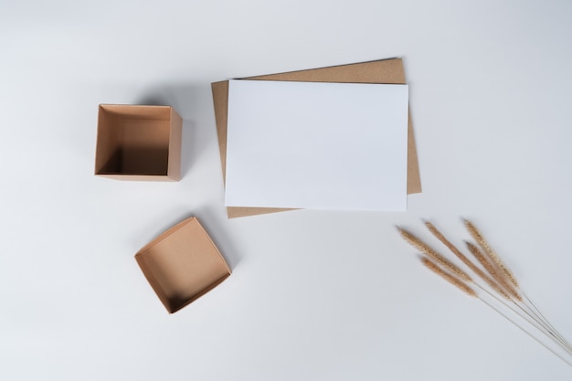 Papier Blanc Vierge Sur Enveloppe De Papier Brun Avec Fleur Sèche Bristly Foxtail Et Boîte En Carton. Vue De Dessus De L'enveloppe De Métier Sur Fond Blanc.