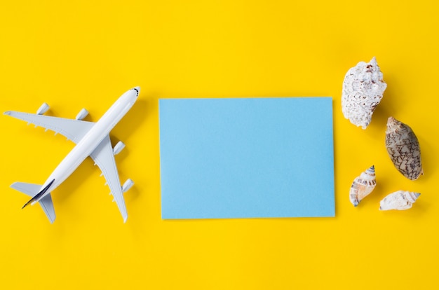 Papier bleu vide sur fond jaune avec des coquillages et avion décoratif. Concept de voyage d'été.