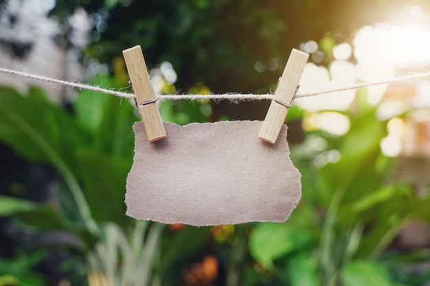 Papier brun vide déchiré ou morceaux déchirés pendus avec des pinces à linge sur corde au jardin vert