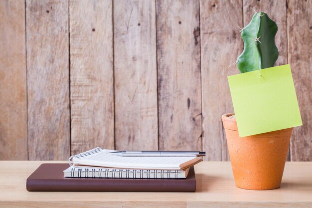 Papier de cahier vierge avec cactus dans des pots en argile sur une image de table en bois utilisée pour ajouter du texte ou un message éducatif