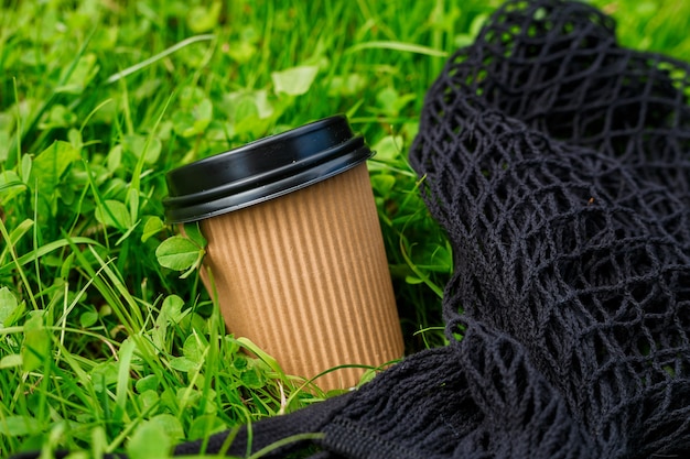 Papier chaud Tasse de café artisanale avec sac noir sur l'herbe un matin. Concept de vente à emporter ou de livraison. Espace de copie. Mode de vie d'été. Placez votre texte ou votre logo sur la tasse, la maquette