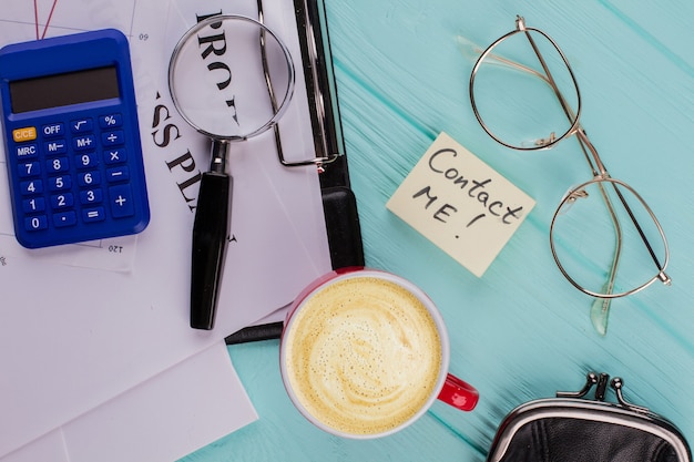 Papier collant avec le mot Contactez-moi sur la table de bureau. Tasse de loupe de verres papiers café portant sur un bureau bleu.