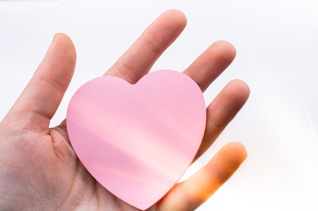 Papier en forme de coeur de couleur rose à la main sur fond blanc