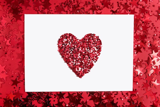 Papier rectangulaire blanc avec un coeur au milieu sur rouge avec des confettis en forme d'étoiles