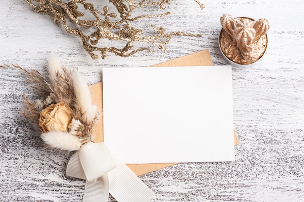 Papier vide et enveloppe kraft avec bouquet de couleurs neutres de fleurs sèches. Succulente dorée et décor sur table blanche. Espace de travail moderne