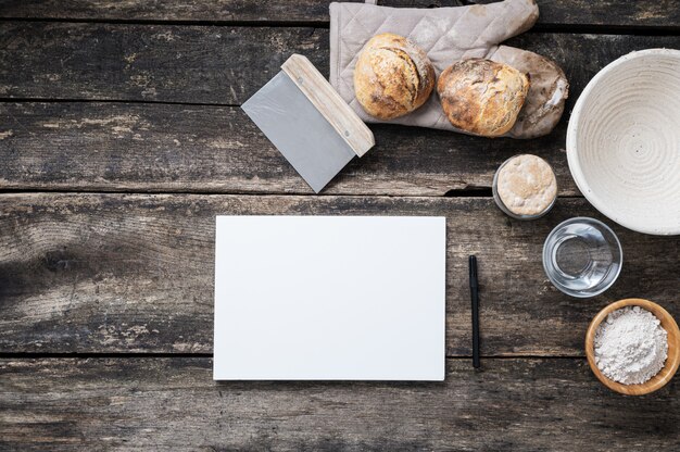 Papier vierge prêt pour une recette écrite à côté du pain et des ingrédients faits maison