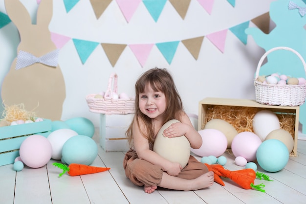 Pâques! Belle petite fille sur un blanc avec des oeufs colorés de Pâques, un panier de Pâques et des lièvres. Décor de Pâques, décorations de printemps à la maison. Vacances en famille, traditions. récolte, petit fermier.