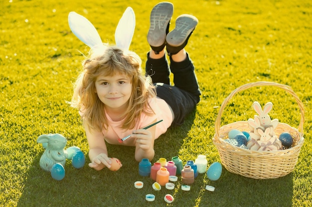 Pâques enfants garçon dans des oreilles de lapin peignant des oeufs de pâques enfant mignon en plein air en costume de lapin avec lapin e