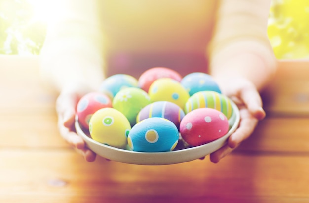 Pâques, fêtes, traditions et concept de personnes - gros plan de mains de femmes tenant des œufs de Pâques colorés sur une assiette