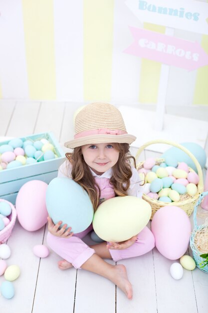 Pâques! fille détient de gros œufs multicolores dans ses mains sur le fond de l'intérieur de Pâques. Un bébé mignon court après les œufs de Pâques. Décoration de Pâques. Enfant et jardin. Petit fermier. Récolte