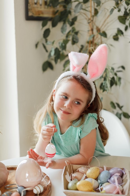 Pâques Une jolie petite fille aux oreilles de lapin décore des oeufs de Pâques à la table à la maison Vacances de printemps