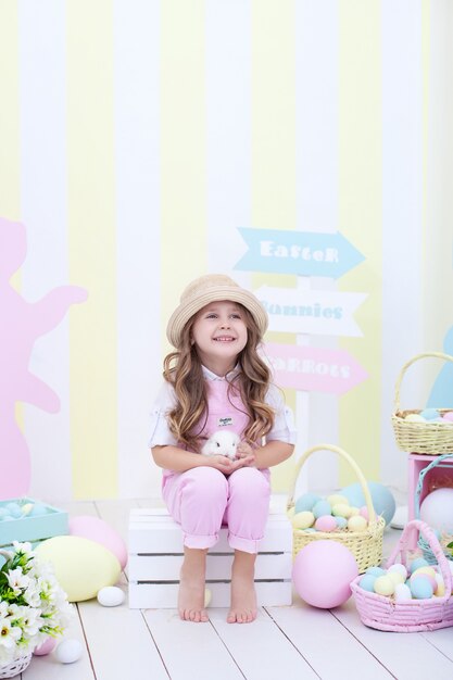 Pâques! petite fille joue avec le lapin de Pâques. Un enfant tient un lapin dans ses bras à l'intérieur de Pâques. Décor coloré de Pâques, agriculture. Enfant et animal. Petit fermier.