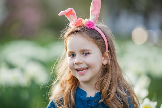 Pâques Petite fille mignonne de 5 ans avec des oreilles de lapin sur la pelouse de jonquilles Enfant heureux Vacances de printemps