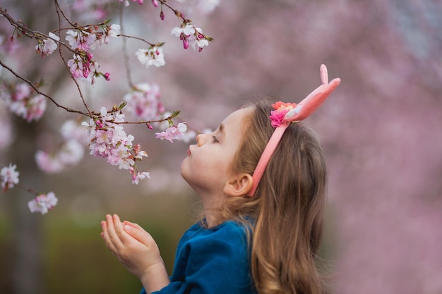 Pâques Petite fille mignonne aux longs cheveux bouclés avec des oreilles de lapin en fleurs de cerisier Vacances de printemps