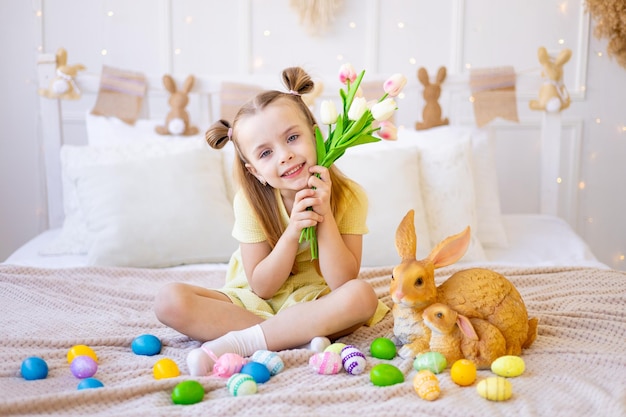 Pâques une petite fille avec des oeufs colorés peints et un lapin tenant des tulipes de fleurs de printemps à la maison dans une pièce lumineuse se préparant pour les vacances en souriant et en s'amusant