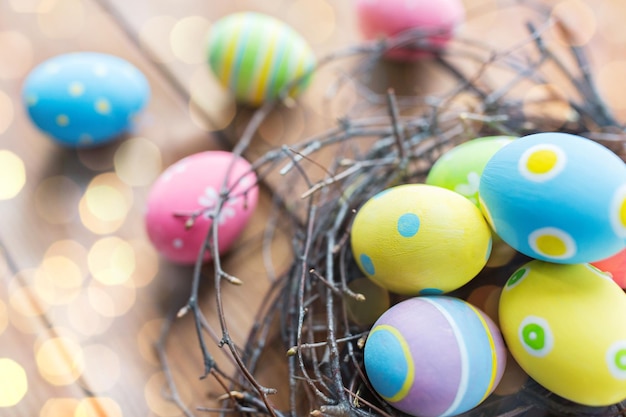 pâques, vacances, tradition et concept d'objet - gros plan d'oeufs de pâques colorés dans un nid sur une surface en bois au-dessus des lumières