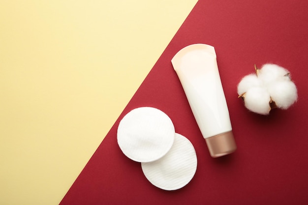 Paquet de crème avec des tampons de coton et fleur sur fond rouge et beige Produits de soin de beauté