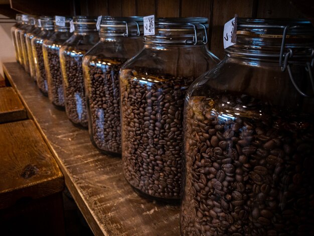 Paquet d'emballage de pot de verre de grains de café noir sur un support en bois à l'arrière-plan de la boutique de café. Grain de café fraîchement torréfié sur bouteille maison.