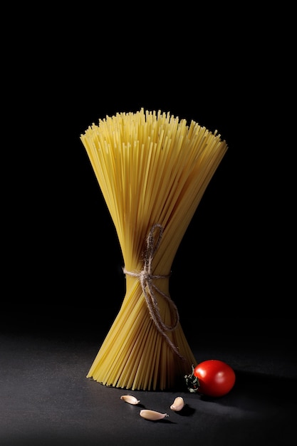 Paquet de pâtes spaghetti à l'ail et tomate cerise sur fond noir.