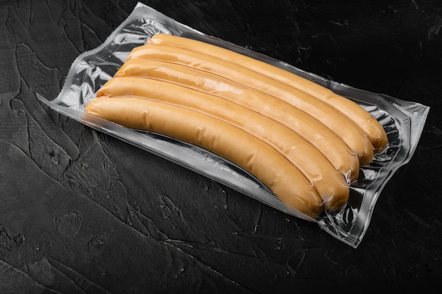 Paquet de saucisses de poulet sous vide sur fond de table en pierre noire foncée avec espace de copie pour le texte