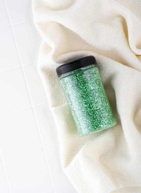 Paquet de sel de cristal de paillettes vertes sur une serviette de salle de bain beige Pot de sel de mer vert scintillant pour spa à domicile Idée d'aromathérapie de relaxation et de soins personnels L'effet de l'eau de mer sur les cheveux