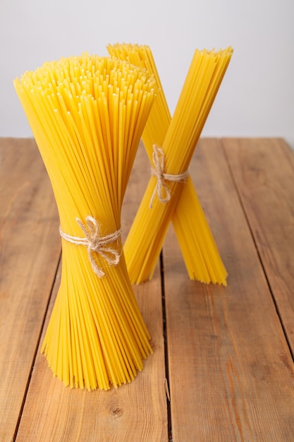 Un paquet vertical et un paquet de spaghettis crus liés avec une ficelle sur un fond en bois