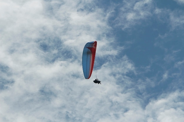 parapente au loin volant avec 2 personnes entre les nuages et le ciel bleu