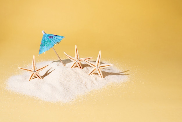 Parapluie bleu avec trois étoiles de mer sur une île de sable sur fond jaune, concept de vacances d'été, gros plan.