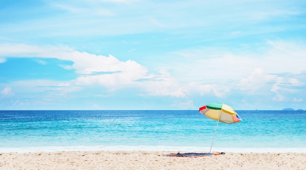 Parapluie coloré sur le sable au-dessus du paysage de ciel et mer bleu.