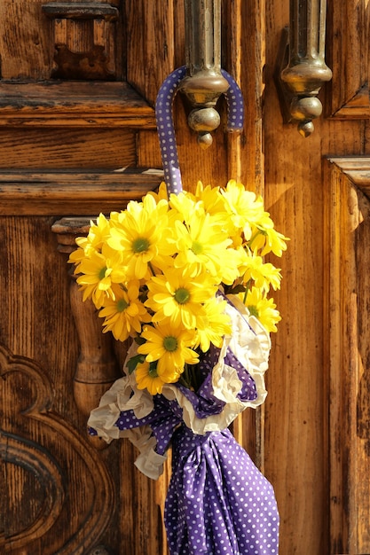 Parapluie de couleur lilas avec de belles fleurs accrochées à une porte en bois