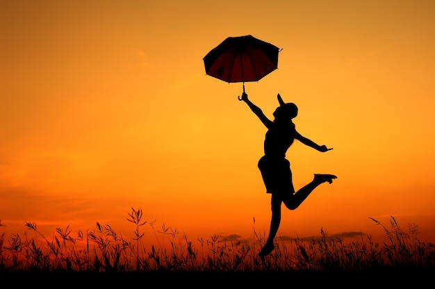 Parapluie femme saut et coucher de soleil silhouette