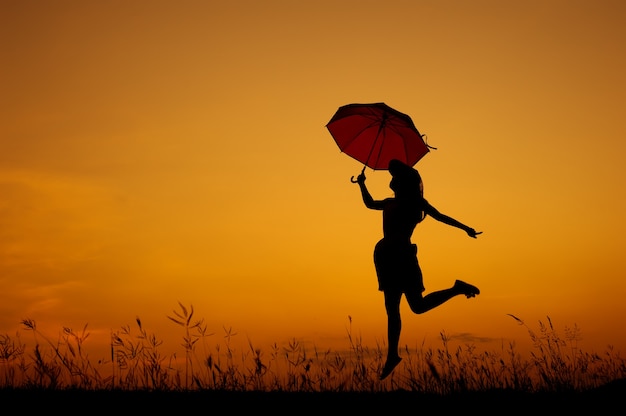 Parapluie femme saut et coucher de soleil silhouette