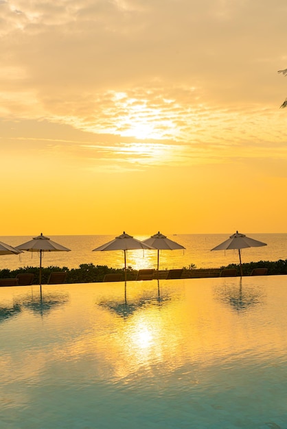parapluie avec lit piscine autour de la piscine avec fond de mer océanique au coucher ou au lever du soleil - concept de vacances et de vacances