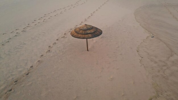 Parapluie de paille solitaire plage vide vue aérienne empreintes de surface de sable beige