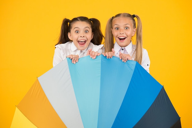 Parapluie surprise. Filles surprises se cachant derrière un parapluie sur fond jaune. Les petits enfants regardent avec surprise. Ouverture des yeux surprise. Retour à l'école surprise.