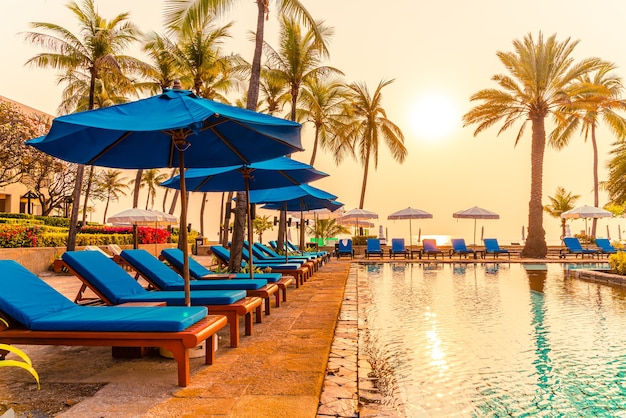 parasol et chaise à la piscine avec des palmiers au lever du soleil