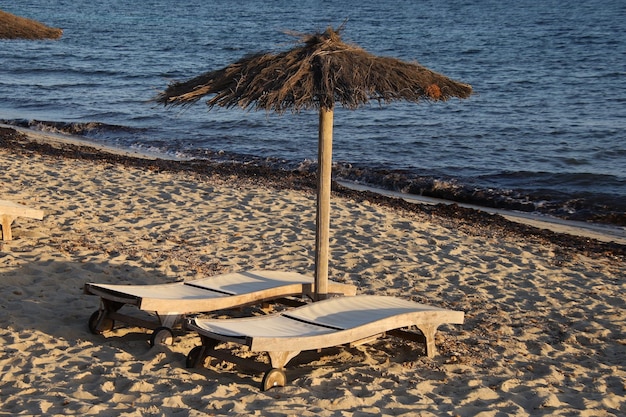 Parasol ouvert en paille avec chaises longues sur le sable de la plage.