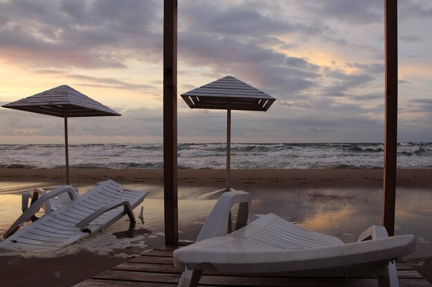 parasols et chaises longues sur le sable mouillé au bord de la plage par temps orageux à la lumière du coucher du soleil