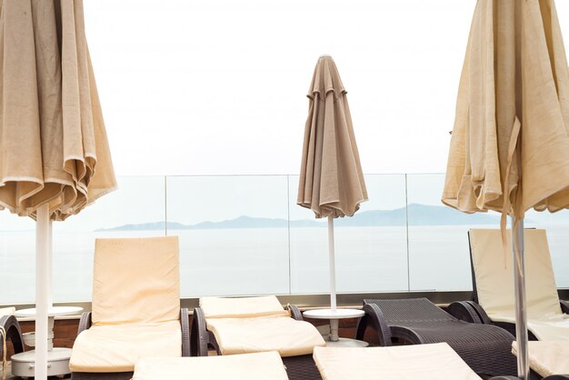 Parasols de couleur beige et chaises longues près de la piscine avec vue sur la mer.